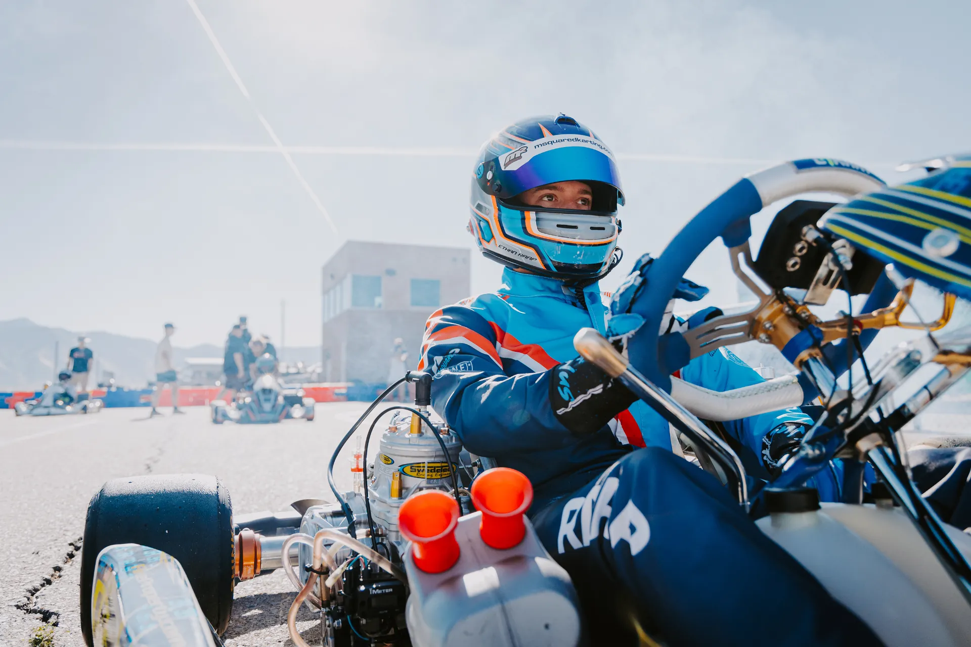 Helmeted karting driver in deep focus moments before the start, waiting on the pre-grid.