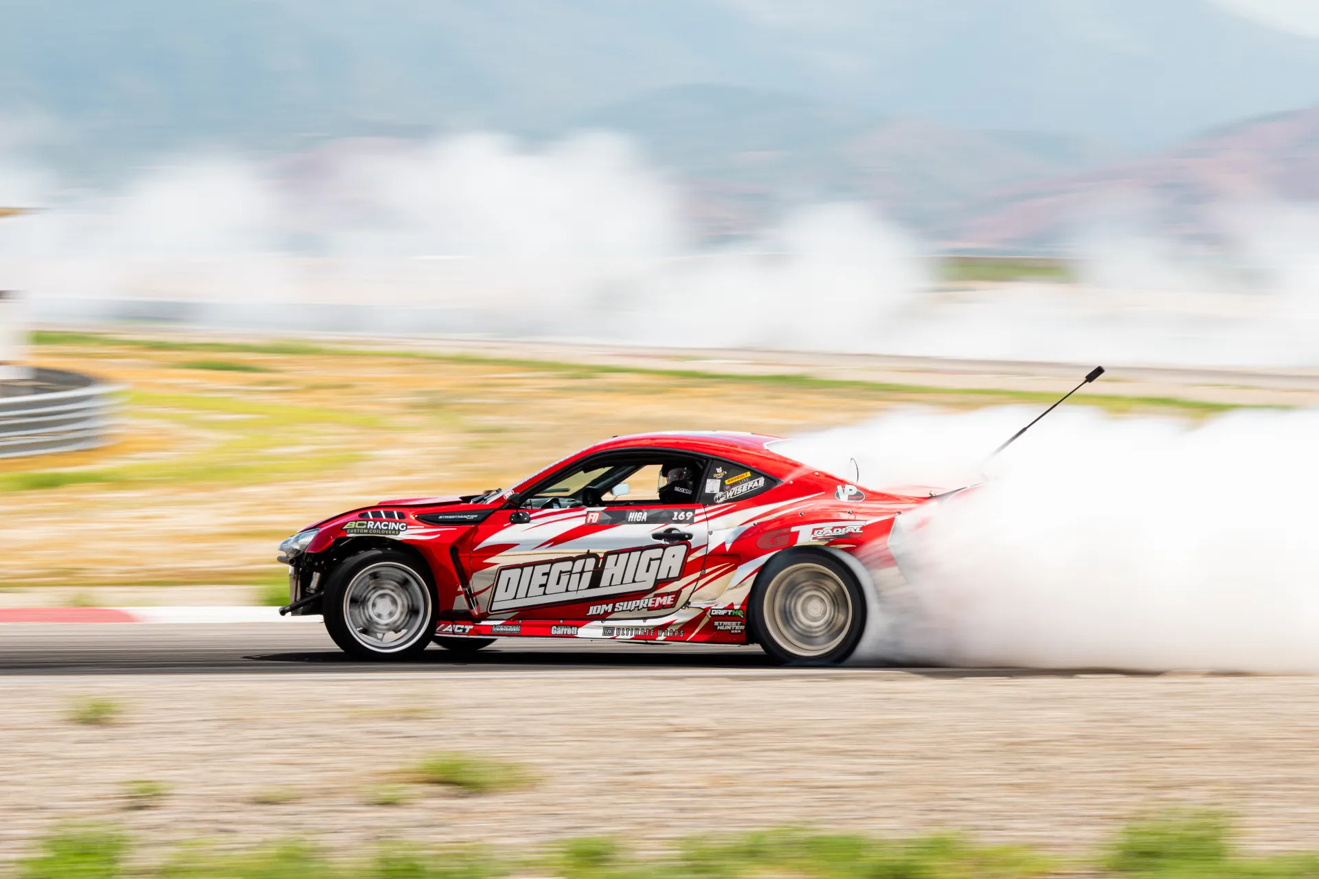 Formula Drift driver Diego Higa sliding sideways in a cloud of tire smoke during competition.