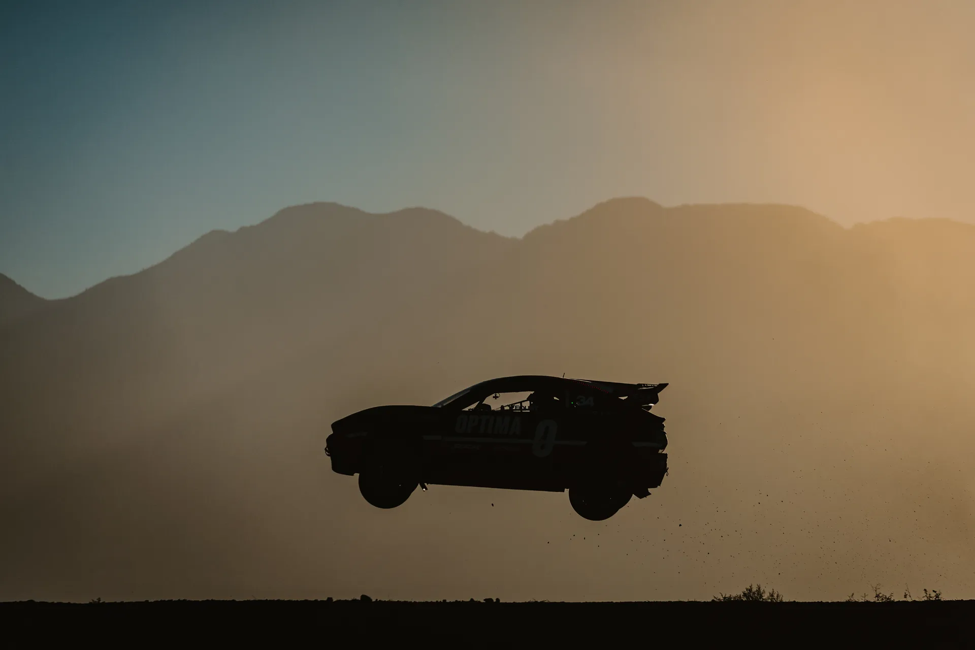 Nitrocross rallycross car silhouetted mid-air over a dirt jump against a golden sunset sky.