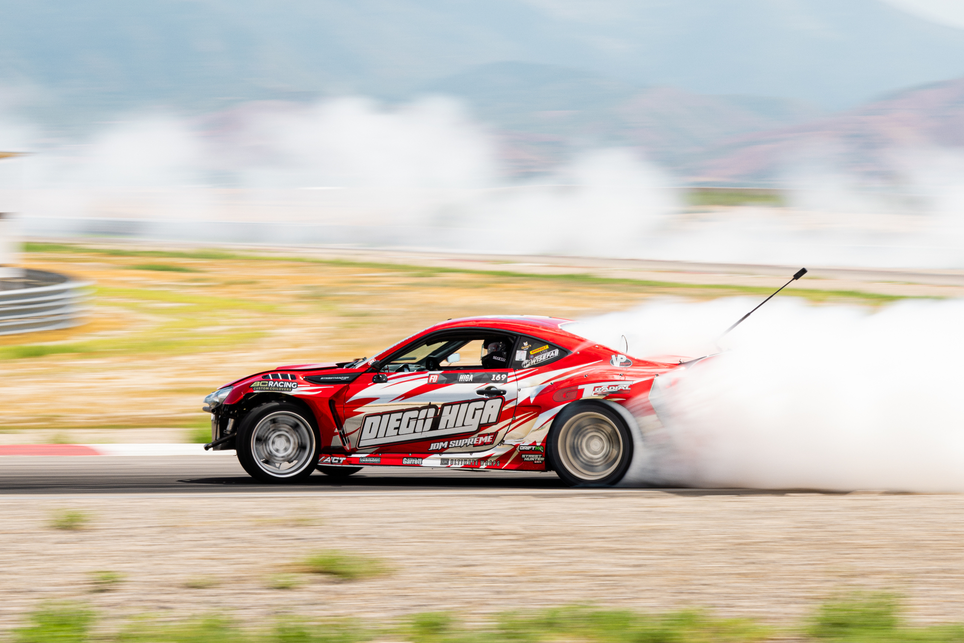 Formula Drift driver Diego Higa sliding sideways in a cloud of tire smoke during competition.