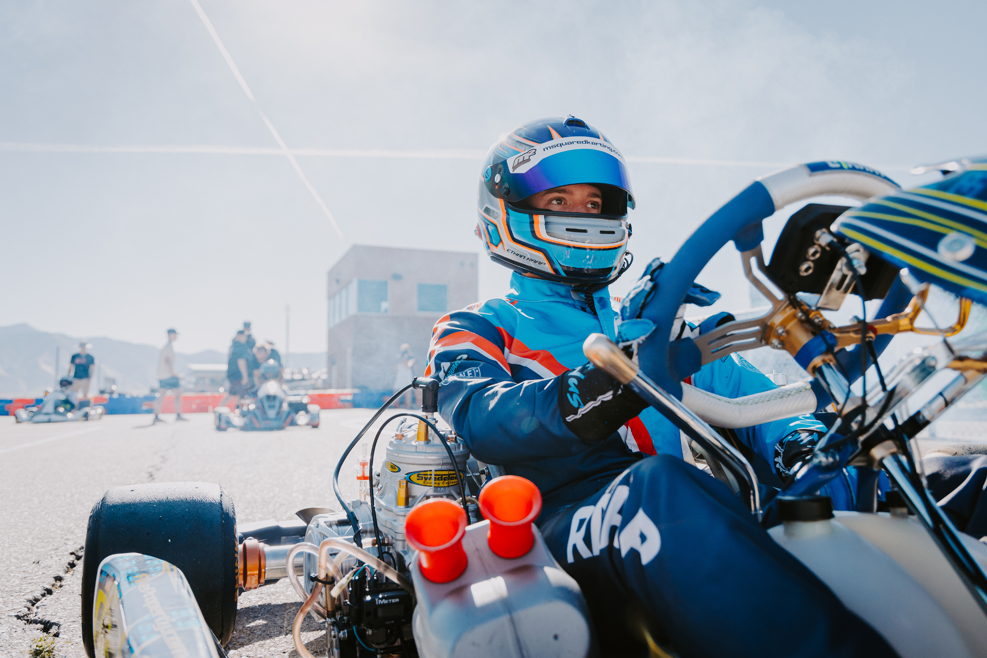 Helmeted karting driver in deep focus moments before the start, waiting on the pre-grid.