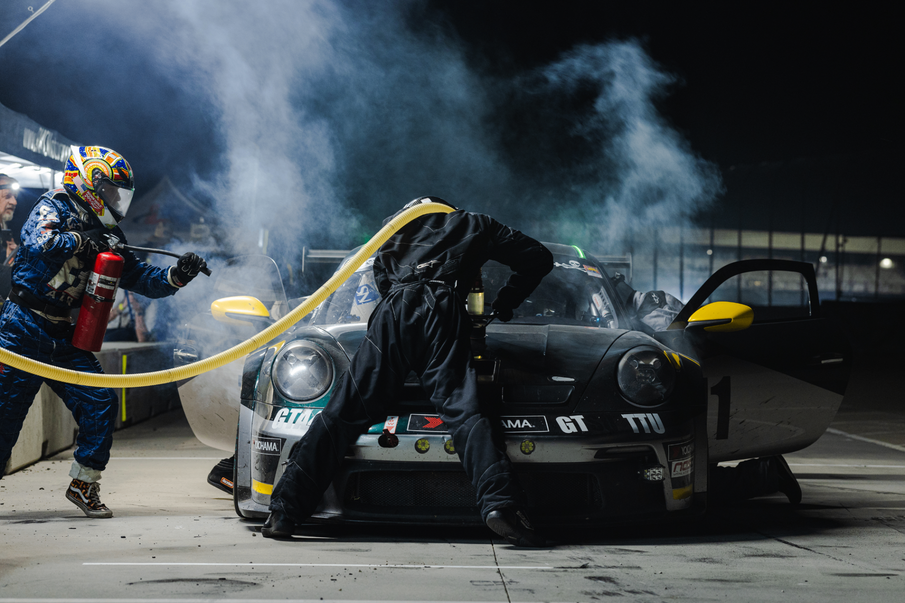 NASA endurance racing crew executing a high-speed pit stop, refueling and changing tires on a race car under track lighting.