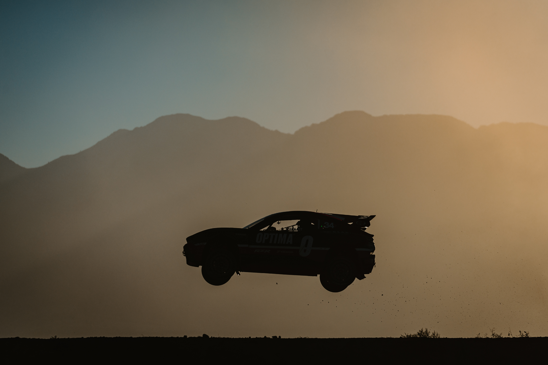 Nitrocross rallycross car silhouetted mid-air over a dirt jump against a golden sunset sky.